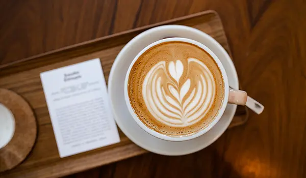 Photographie culinaire réalisée par Speetch au café "Ça passe crème" à Lausanne : gros plan sur un latte art minutieux dans une tasse de café, présenté sur un plateau en bois.