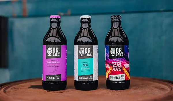 Photographie de produits culinaires par Speetch : trois bouteilles de bières artisanales Dr. Gab's posées sur un tonneau, photographe pour entreprises à Yverdon.