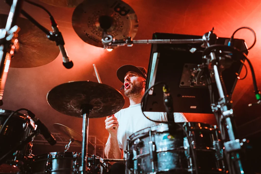 Photographie de concert par Speetch au Venoge Festival (Vaud) : le batteur du groupe de reggae Dub Inc. en pleine performance sous des projecteurs rouges, reportage événementiel en Suisse romande.