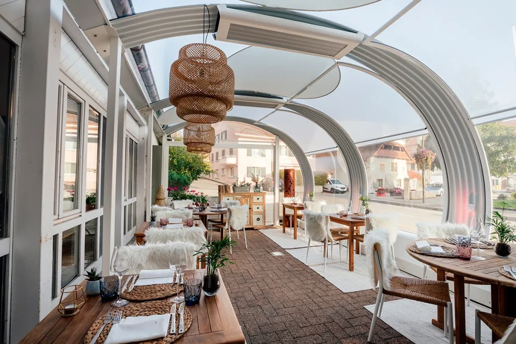 Photographie d'architecture et design d'intérieur par Speetch : terrasse de restaurant lumineuse sous une structure moderne courbée, décoration chaleureuse dans le Canton de Vaud.