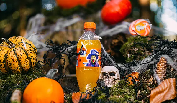 Photographie publicitaire par Speetch : mise en scène d'une bouteille de Fanta pour Halloween avec citrouilles, crânes et toiles d'araignée en Suisse romande.